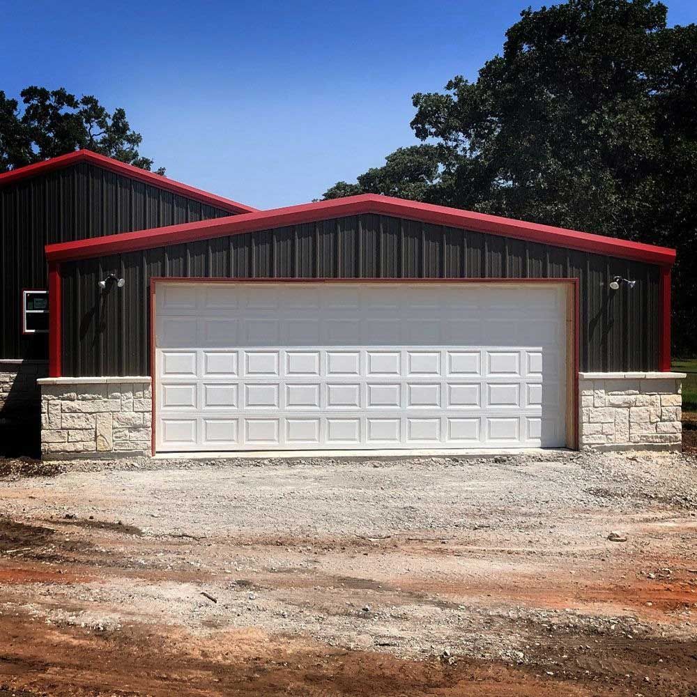 Garage with white door, black metal siding, red trim, and stone accents under a blue sky.