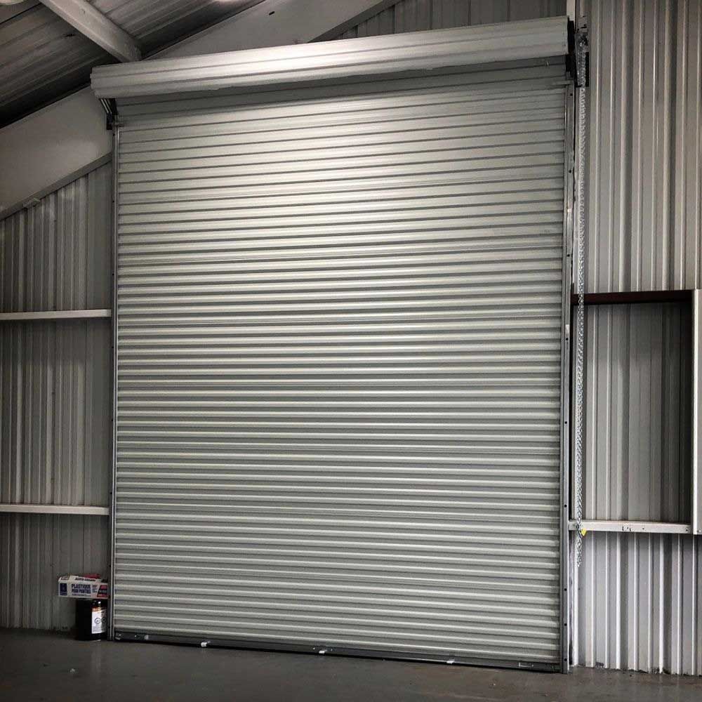 Metal roll-up door in a building, closed. Gray corrugated metal, with a dark gray interior.