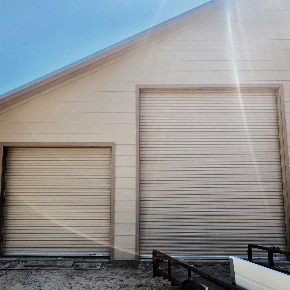 Beige industrial building with two closed roll-up garage doors, under a bright blue sky.