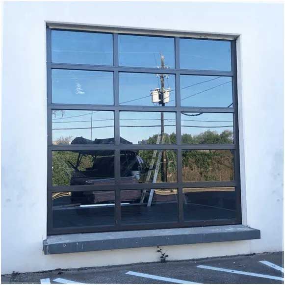 Large, reflective window with dark gray frame on a white building. Reflects outdoor scene with utility pole.