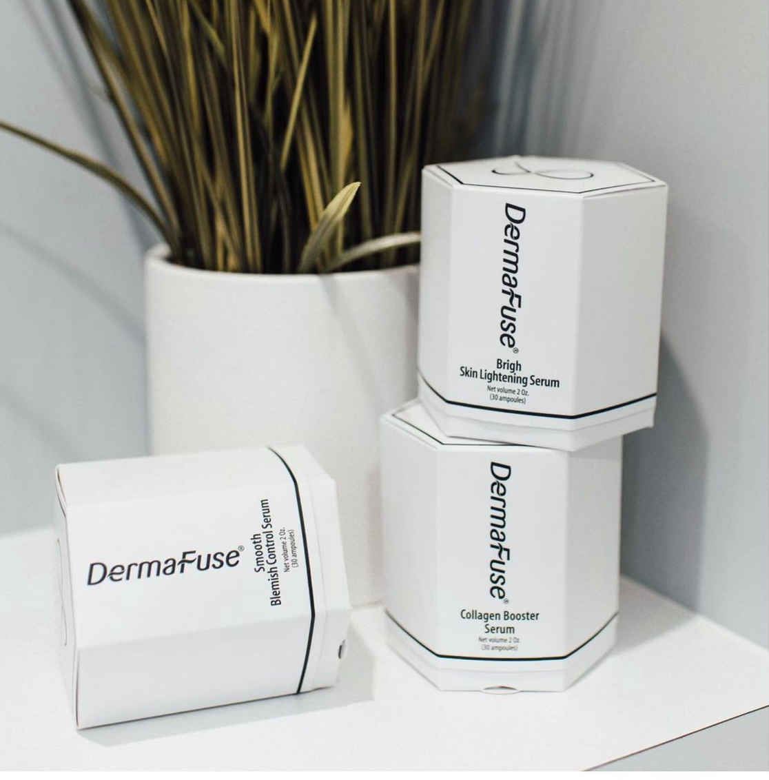 Three white DermaFuse product boxes stacked on a table, with a plant in a white vase behind them.