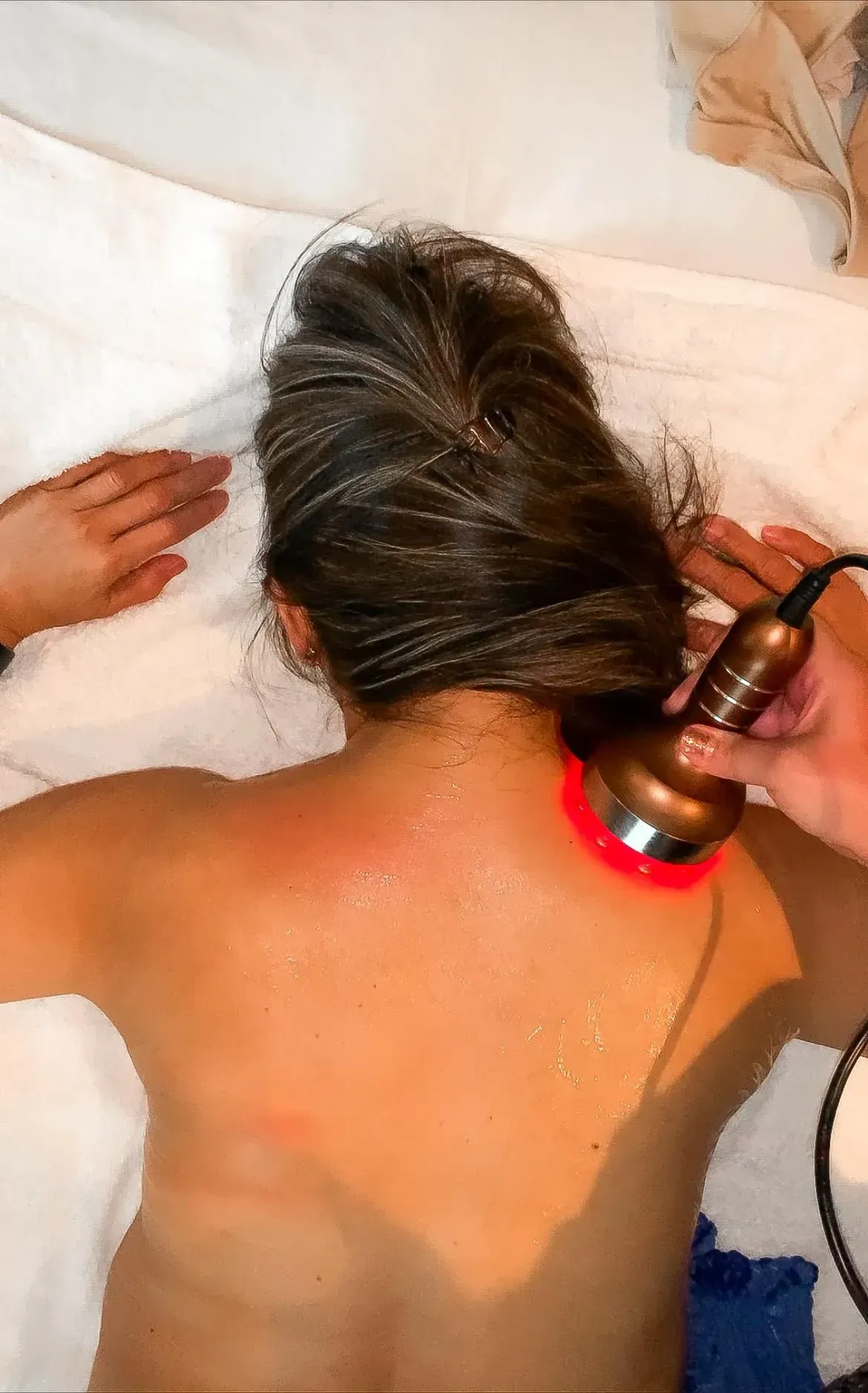 Woman receiving red light therapy on her back; device held near shoulder.