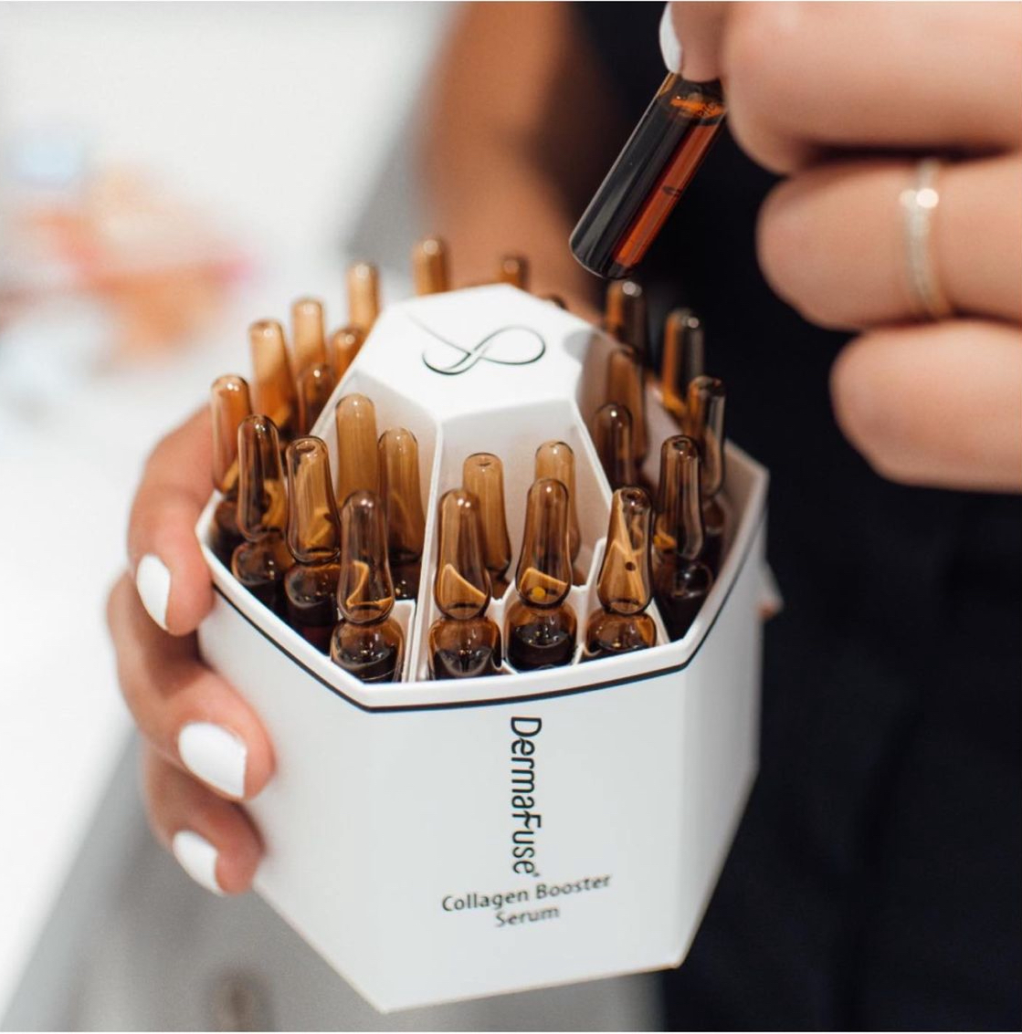 Woman holding box of DermaFuse collagen booster serum ampoules. Brown vials in white box, with hand holding one.
