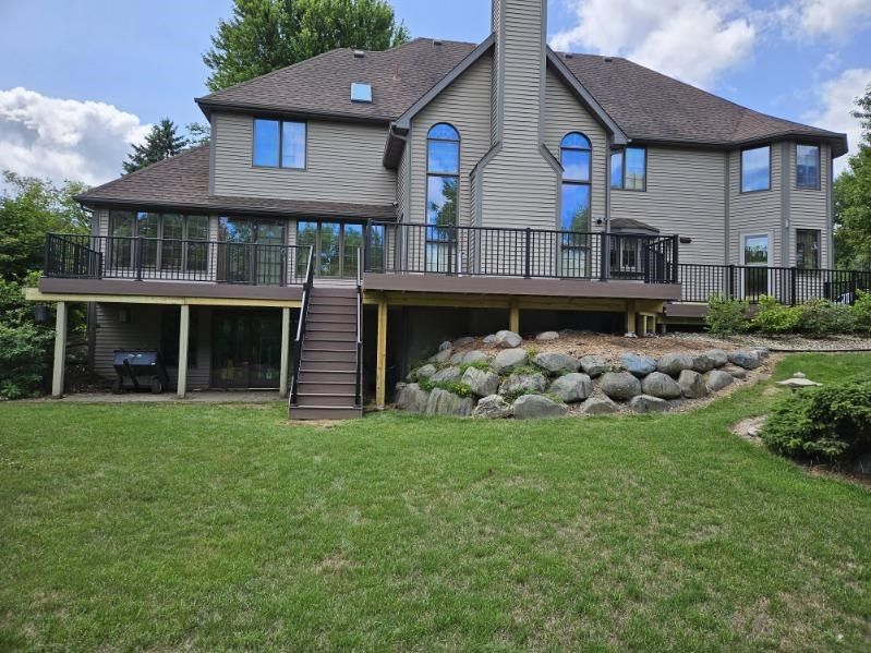 Back of a two-story beige house with a brown deck, stairs, and a grassy lawn.