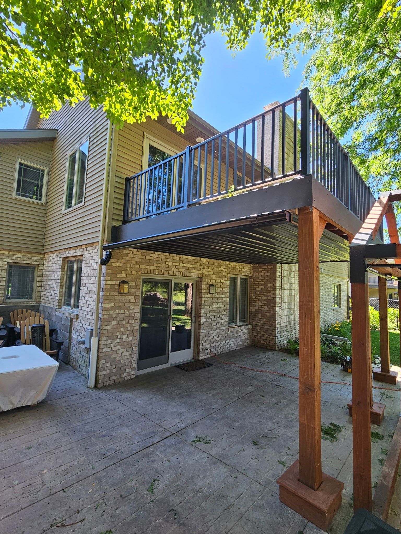 Backyard deck with stairs, stone house exterior, and large tree overhead