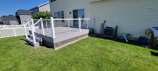 A gray deck with white railing next to a house with a person working on the side.