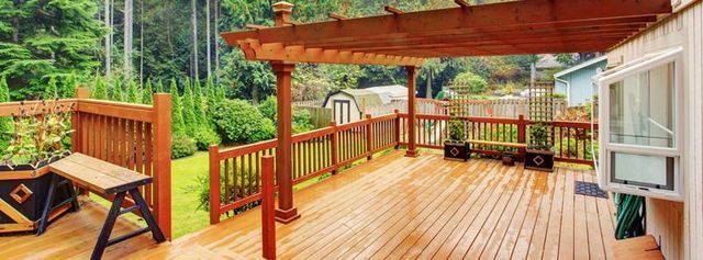 Wooden deck with a pergola, overlooking a lush green yard.