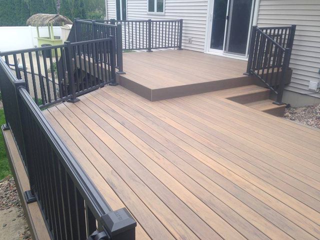 Wooden deck with black railings and steps leading down to a lower level next to a house with sliding glass doors.