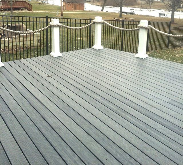 Gray composite deck with rope railing and black fence.