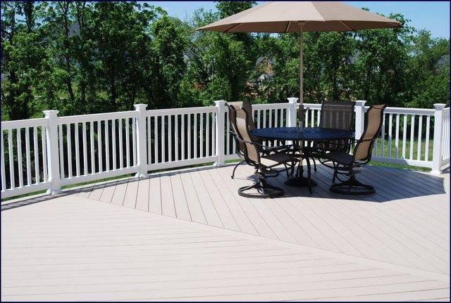 White railed deck with round table, chairs, and umbrella, overlooking a green tree filled yard.