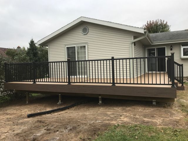 Brown composite deck with black railing attached to a beige house, set in a grassy yard.