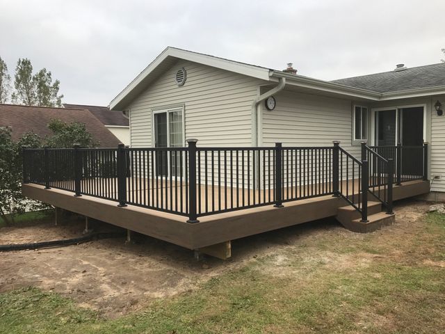Composite deck with black railing next to a house with sliding glass doors.