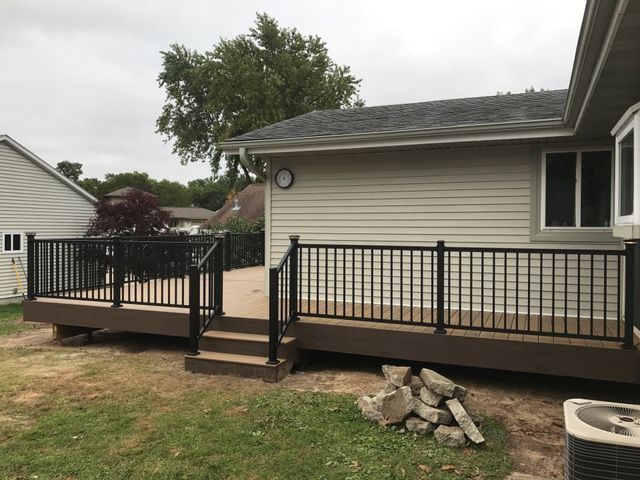 Deck with black railings and brown decking next to a house with beige siding, set in a backyard.