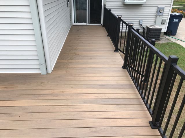 Brown deck with black railing next to a gray house, leading to sliding glass doors.