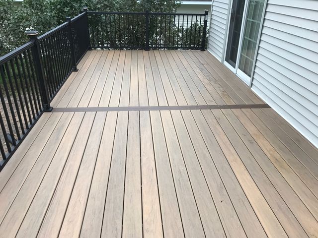 Wooden deck with black railing next to a house with sliding glass door.