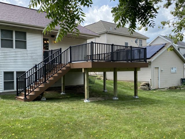 Elevated wooden deck with black railings and stairs, attached to a house and overlooking a grassy yard.