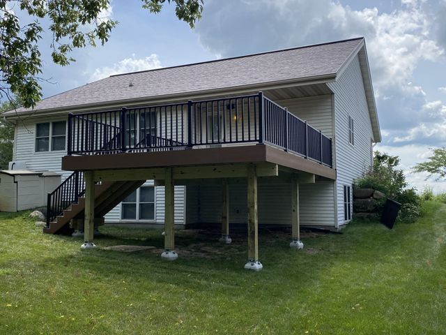 Two-story white house with a brown deck and black railings. Deck supported by wooden posts on a grassy lawn.