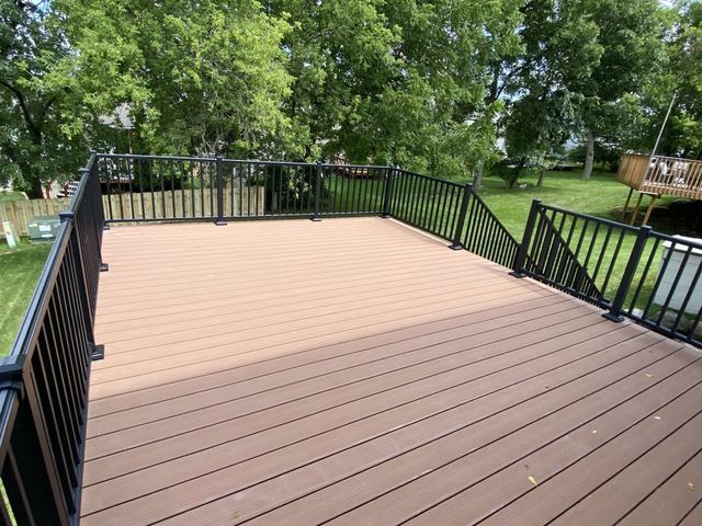 Elevated deck with brown composite boards and black railings, overlooking a yard with trees.