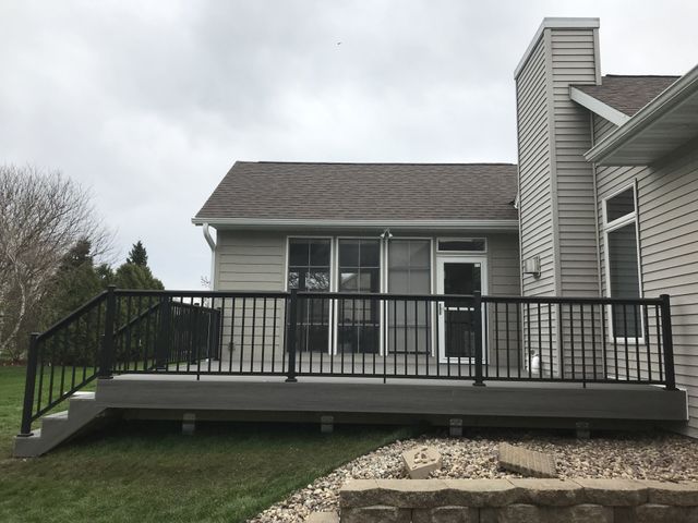 Deck with black railing, gray composite decking, and house in background on a cloudy day.