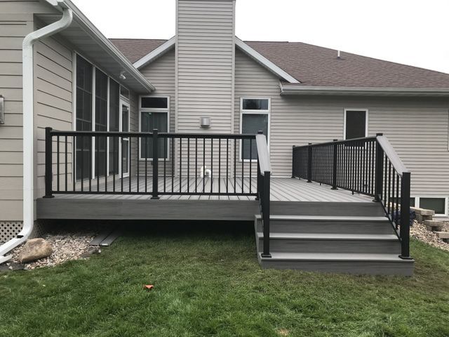 Gray composite deck with black railings and steps leading to lawn. House exterior in background.