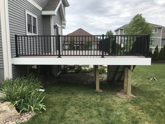 Deck with black railings attached to a gray house, set in a grassy yard.