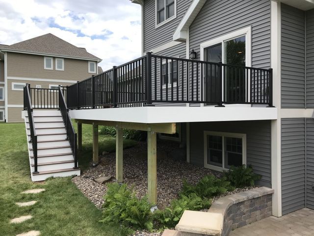 Black railing and stairs on a deck attached to a gray house, with a lawn.