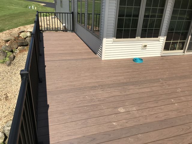 Brown composite deck with black railing next to a sunroom, overlooking a yard with rocks.