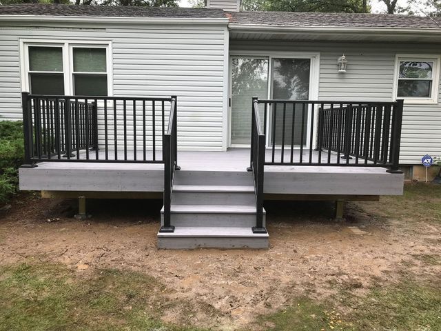 Gray deck with black railing and steps leading to a sliding glass door; outdoors.