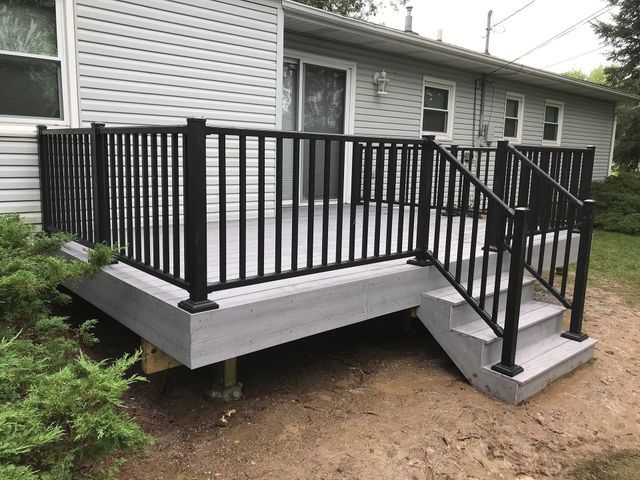 Gray deck with black railing and steps attached to a house with vinyl siding.