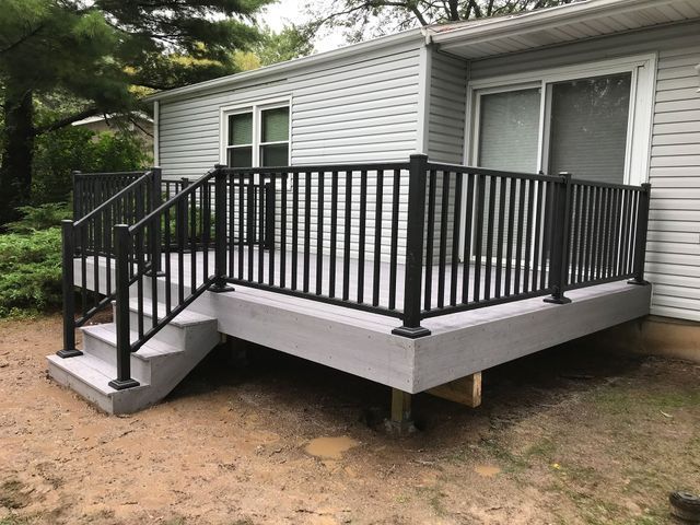 Gray deck with black railing and steps attached to a light gray house.