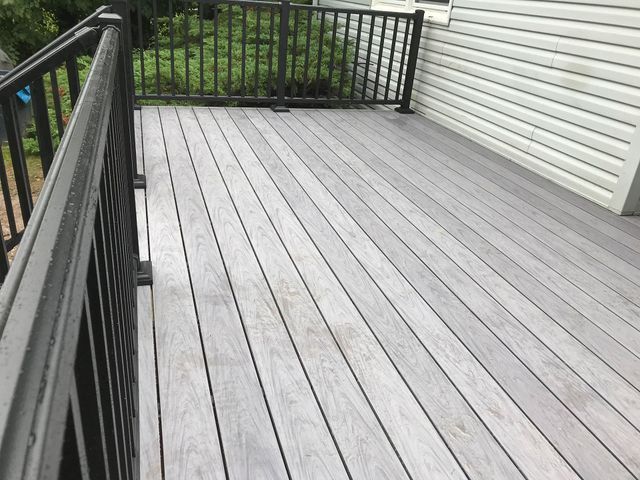 Gray composite deck with black railing next to a white house with trees in the background.