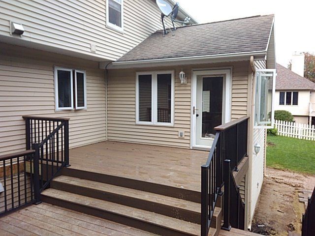 A wooden deck with steps leading down from a beige house. Black railings and windows surround the deck.