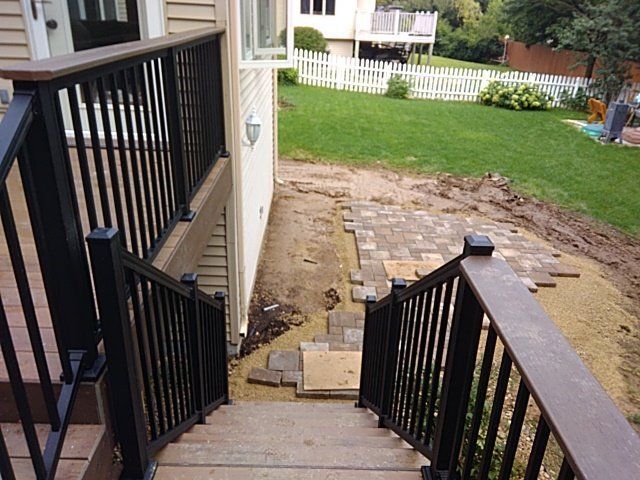 Wooden deck with black railings and steps leading to a brick patio area under construction.