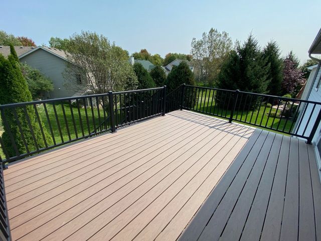 Composite deck with black railing overlooking a green lawn and houses under a blue sky.