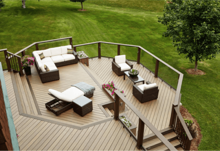 Wooden deck with outdoor furniture on a grassy hill. Includes a sectional, chairs, and coffee table.