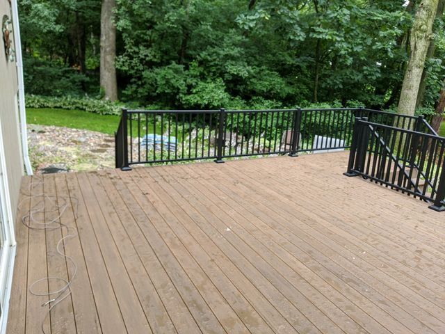 Wooden deck with black railing overlooking a green yard and trees.