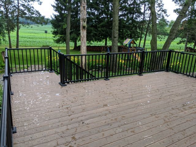 A wooden deck with black railings overlooks a backyard with trees and a playground.