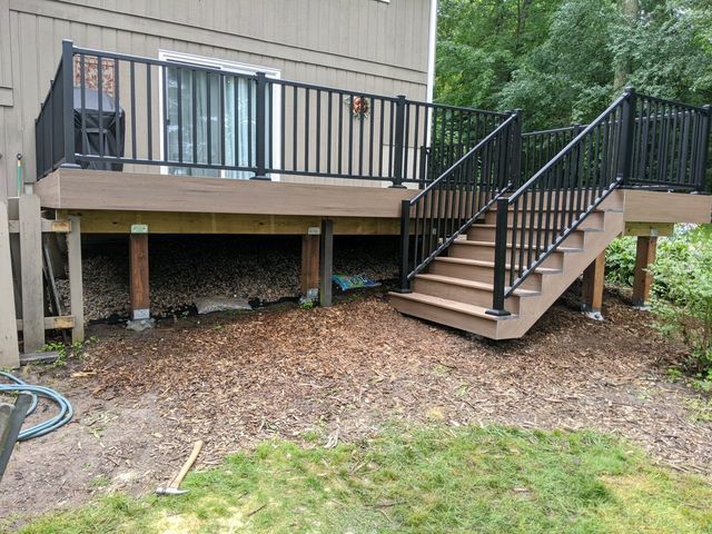 Deck with black railings, stairs, and brown composite decking. Supports are visible below.