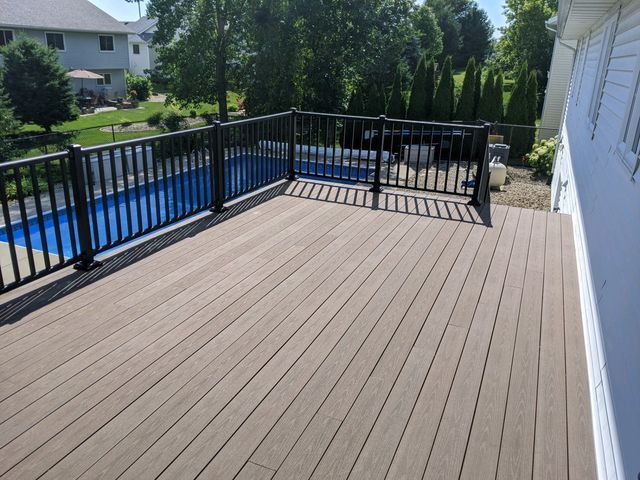 Composite deck with black railing overlooking a blue swimming pool on a sunny day.