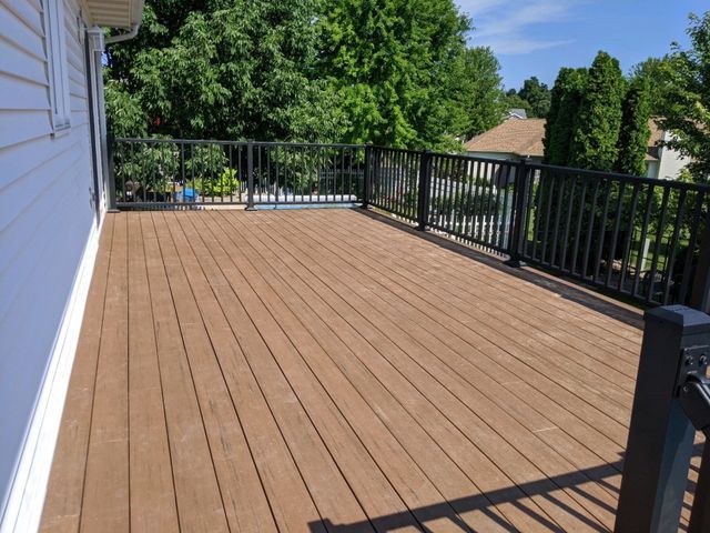 Wooden deck with black railings overlooking a green tree-filled yard.