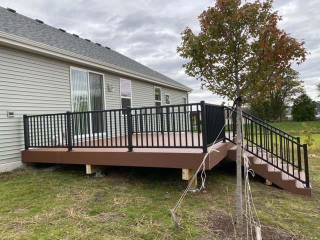 Brown composite deck with black railing and steps attached to a light gray house.