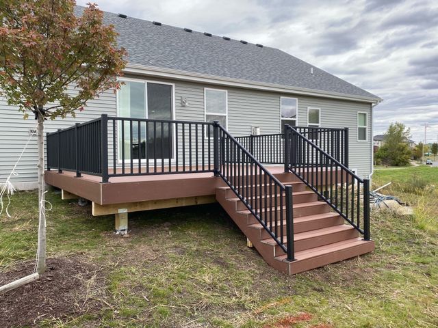 Brown deck with black railing and stairs attached to a light gray house.