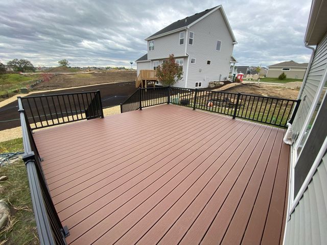 Brown composite deck with black railing and two-story house in background under cloudy sky.
