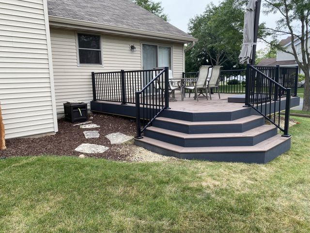 A multi-level composite deck with black railings and steps in a backyard, beside a house.