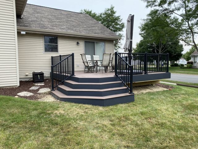 A deck with dark gray steps and black railing; chairs and a patio umbrella on the deck.