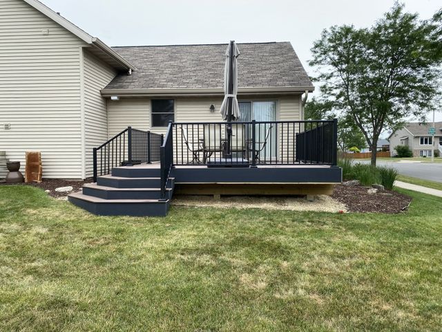 Deck with black railing and steps attached to a house with a sliding glass door.