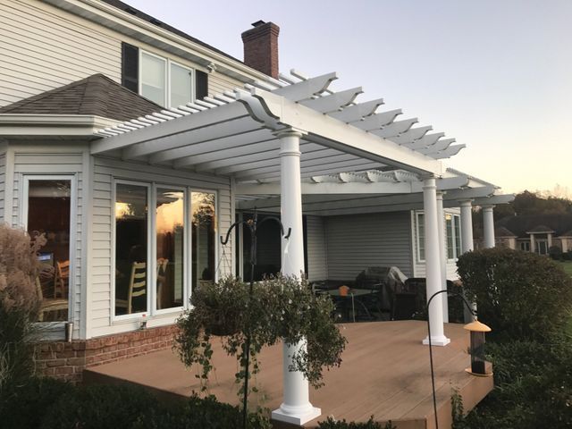 White pergola attached to a light-colored house over a patio. Late afternoon light.
