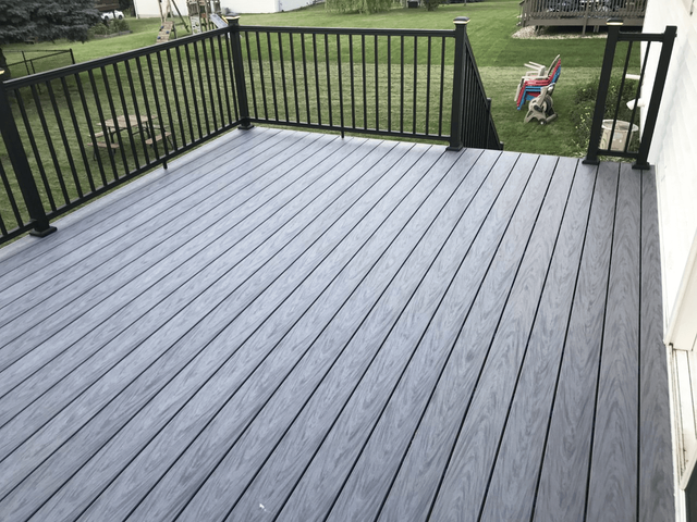 Gray composite deck with black railing in a grassy backyard.