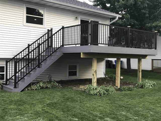 A house with a gray deck and stairs, black railings, and a black door.