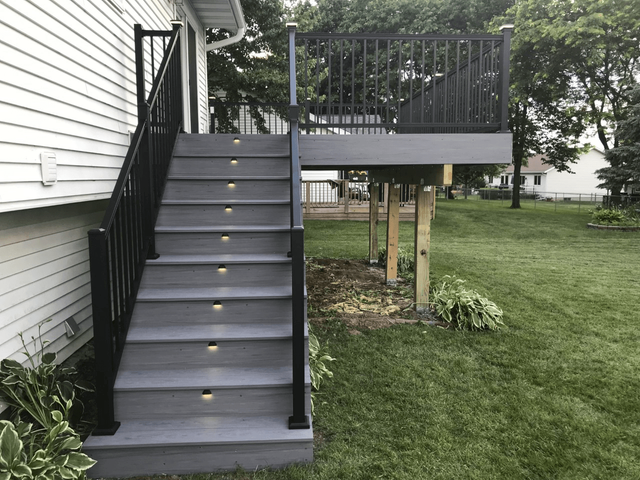 Gray deck with black railing and steps leading down to yard with built-in lights.